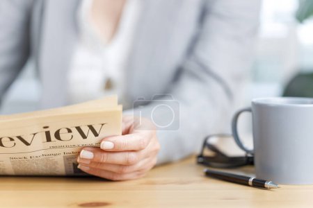 Foto de Primer plano de la mujer de negocios leyendo el periódico en el escritorio de la oficina. Enfoque selectivo en el periódico. Negocios, finanzas, economía - Imagen libre de derechos