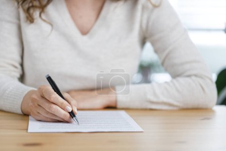 Photo for Close-up shot of an unidentifiable young woman filling out paperwork at her work desk - Royalty Free Image