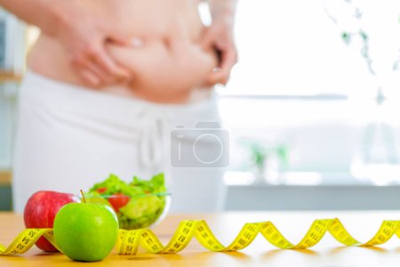 Téléchargez les photos : Pomme rouge et verte avec ruban à mesurer sur la table avec corps gras féminin à l'arrière-plan pour la conception de régime - en image libre de droit