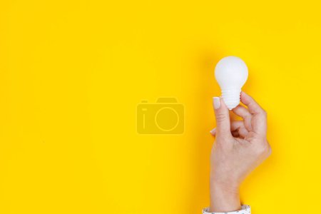 Photo for Woman hand holding a white light bulb on yellow background - Royalty Free Image