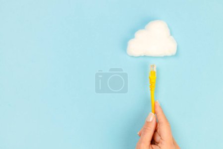 Photo for Woman hand holding connection cable towards the cloud on blue background. Internet connection and cloud technology - Royalty Free Image