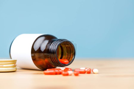Téléchargez les photos : Flacon de médicament et pilules rouges sur table en bois. Les pilules se répandent sur une table en bois. - en image libre de droit