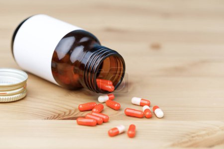Photo for Medicine bottle and red pills on wooden table. The pills spill onto a wooden table. - Royalty Free Image