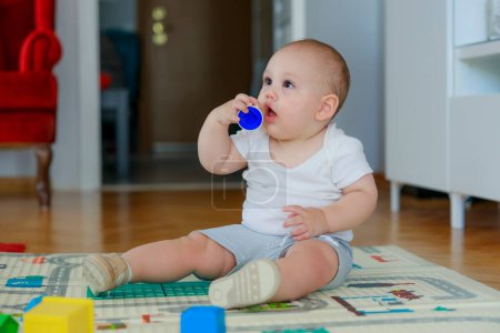 Photo for Baby boy sitting in living room. He is looking around while playing with toys - Royalty Free Image