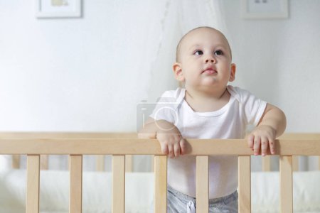 Photo for Portrait of a cute baby boy standing in his crib. Smiling happy little toddler boy stand in the baby cot - Royalty Free Image