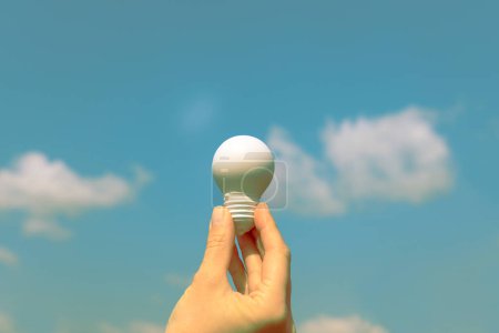 Photo for Woman's hand holding a white light bulb against the blue sk - Royalty Free Image