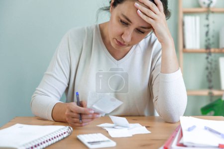 Sad depressed young woman holding bills, having problems with dismissal at home office. Expensive charges on domestic bills. Woman worried about financial problems.