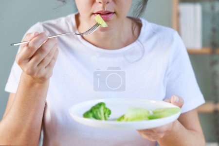 Téléchargez les photos : Problèmes de régime. Trouble alimentaire. Une jeune femme qui mange des légumes frais. La malnutrition nuit à la santé - en image libre de droit