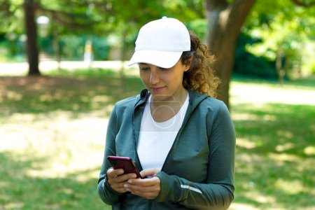 Téléchargez les photos : Jeune athlète femme utilisant téléphone mobile après l'entraînement de course en plein air - en image libre de droit