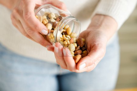 Photo for Nuts spilling from jar in woman's hand - Royalty Free Image