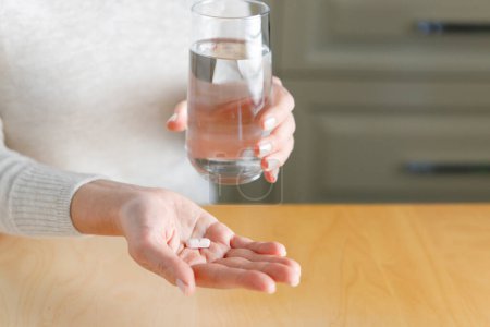 Téléchargez les photos : Gros plan d'une femme méconnaissable tenant un verre d'eau et des médicaments dans la kitche - en image libre de droit