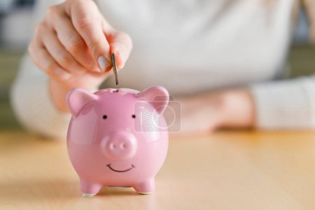Photo for Woman putting money into piggy bank. Concept of money saving and budgeting. Saving money with pink cute piggy bank - Royalty Free Image
