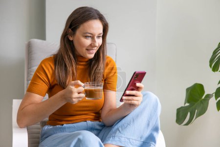 Photo for Young woman using mobile phone while sitting a sofa at home - Royalty Free Image