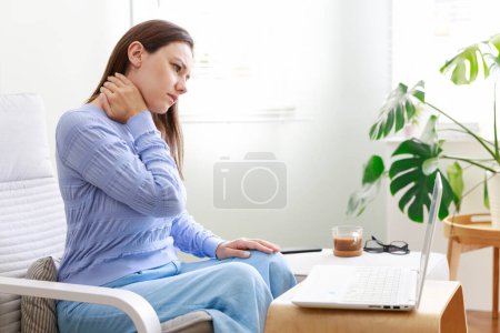 Téléchargez les photos : Freelance jeune femme souffrant de douleur au cou tout en travaillant sur ordinateur à la maison - en image libre de droit