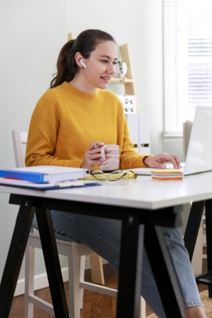 Foto de Retrato de una mujer joven con auriculares usando una computadora portátil, sentada en la oficina en casa y haciendo una videoconferencia - Imagen libre de derechos