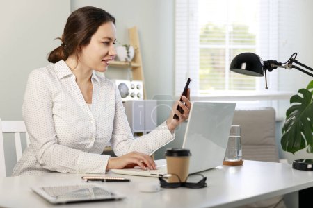 Foto de Joven mujer de negocios que trabaja en el ordenador portátil y el uso de teléfonos inteligentes en casa. Conjunto de trabajo independiente - Imagen libre de derechos