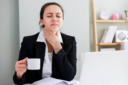 Foto de Joven mujer de negocios con dolor de garganta trabajando con computadora en la oficina - Imagen libre de derechos