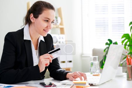 Téléchargez les photos : Une femme d'affaires dans son bureau à domicile faisant du shopping en ligne et payant pour des choses sur son portable - en image libre de droit