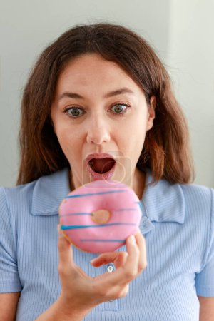 Foto de Hermosa mujer joven comiendo rosado chispas de chocolate donut con una cara feliz - Imagen libre de derechos