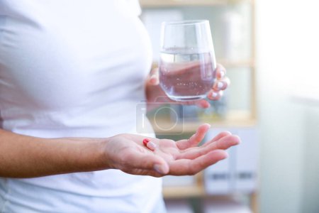Photo for Closeup shot of an unrecognisable woman holding a glass of water and medication in the roo - Royalty Free Image