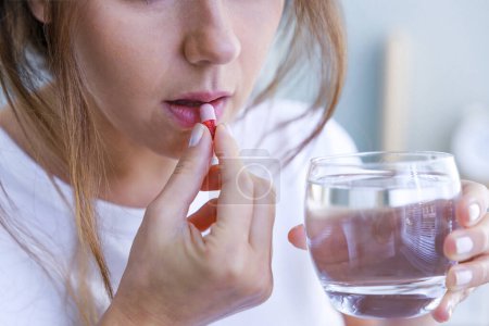 Téléchargez les photos : Femme malade utilisant des antibiotiques avec un verre d'eau dans les mains - en image libre de droit