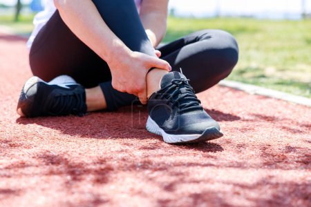 Téléchargez les photos : Jeune femme assise dans l'athlétisme et souffrant d'une blessure à la cheville pendant son entraînement - en image libre de droit