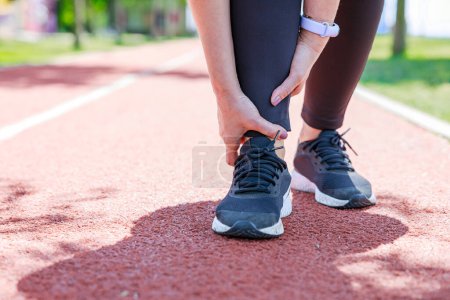 Photo for Injury from workout: Young woman use hands hold on her ankle while running on track fiel - Royalty Free Image
