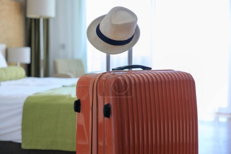 Foto de Maleta de color naranja y un sombrero de paja entregado de pie en la habitación de hotel - Imagen libre de derechos