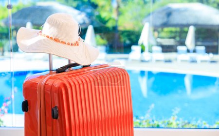 Téléchargez les photos : Valise en chambre d'hôtel contre paysage de piscine. Valises et chapeau de paille estivale en bungalow dans un resor touristique tropical - en image libre de droit
