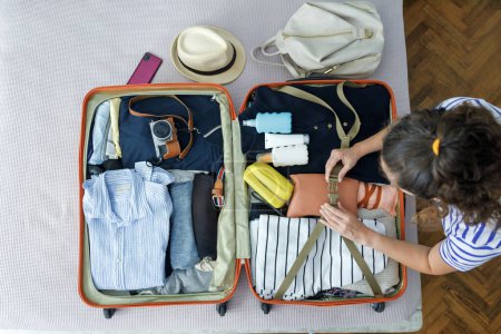 Téléchargez les photos : Jeune femme valise d'emballage pour les voyages d'été, y compris la crème solaire et la caméra - en image libre de droit