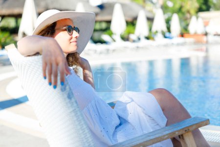 Photo for Smiling young woman lying back in a poolside lounge chair - Royalty Free Image