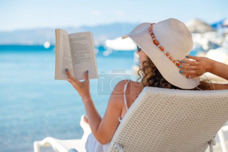 Foto de Retrato de una joven con sombrero de paja, relajante en la playa, leyendo un libro - Imagen libre de derechos