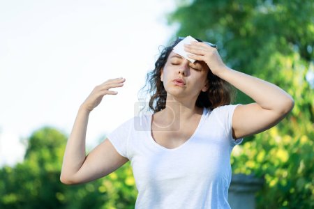 Photo for Young woman having hot flash and sweating in a warm summer day. Woman drying with paper napkin in too hot weather - Royalty Free Image