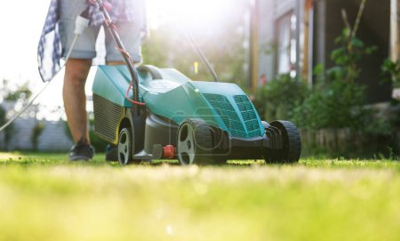 Photo for Young man in his backyard mowing grass with a lawn mower on a sunny day - Royalty Free Image
