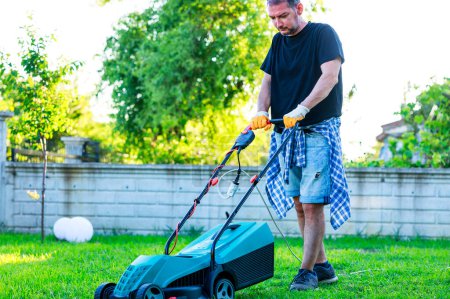Foto de Joven en su patio trasero cortando hierba con una cortadora de césped en un día soleado - Imagen libre de derechos