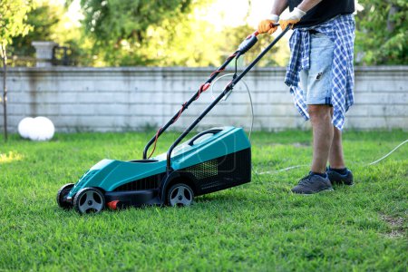 Photo for Young man in his backyard mowing grass with a lawn mower on a sunny day - Royalty Free Image
