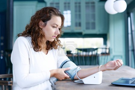 Foto de Mujer autónoma midiendo su presión arterial sintiéndose mal mientras trabaja en su computadora portátil - Imagen libre de derechos