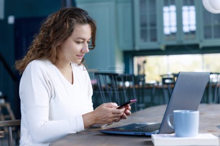 Téléchargez les photos : Jeune femme d'affaires travaillant sur un ordinateur portable et utilisant un smartphone à la maison. Concept de travail indépendant - en image libre de droit