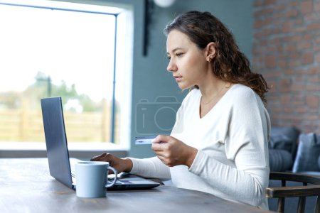 Téléchargez les photos : Une femme d'affaires dans son bureau à domicile faisant du shopping en ligne et payant pour des choses sur son ordinateur portable - en image libre de droit
