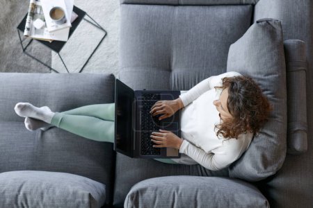Photo for Top view of young woman sitting on sofa at home with laptop - Royalty Free Image