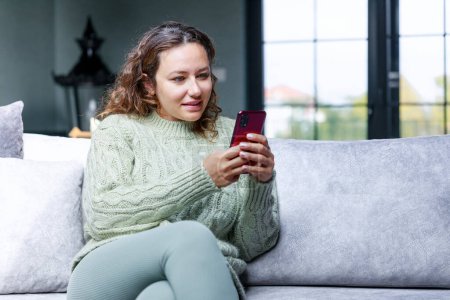 Foto de Mujer joven usando el teléfono móvil mientras está sentado en un sofá en casa - Imagen libre de derechos
