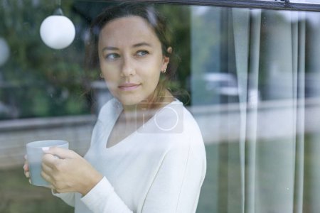Foto de Mujer adulta tomando café y mirando por la ventana - Imagen libre de derechos