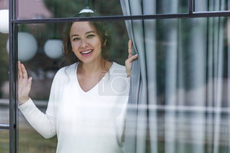 Foto de Sonriente mujer adulta en casa mirando por la ventana - Imagen libre de derechos