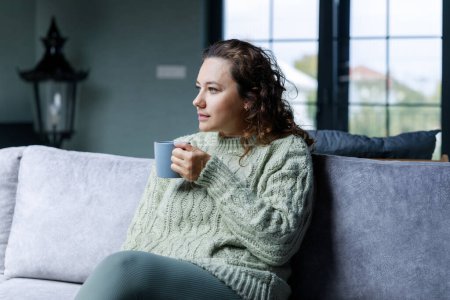 Photo for Young woman sitting on the sofa drinking coffee. Leisure activity, lifestyle for people concept - Royalty Free Image