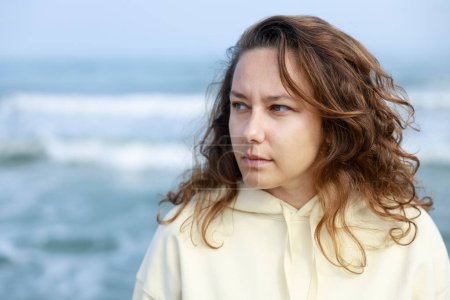 Foto de Mujer joven en un estado de ánimo preocupado e irritable solo junto al mar en otoño - Imagen libre de derechos