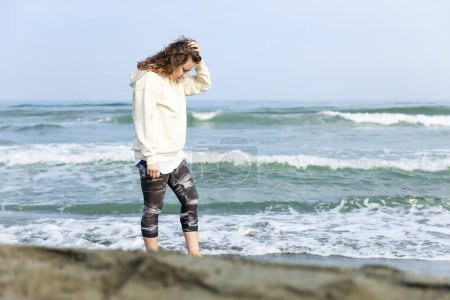Foto de Mujer joven preocupada caminando en la playa cerca del mar - Imagen libre de derechos