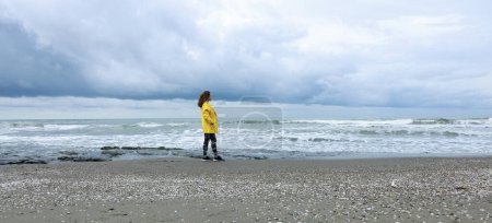 Foto de Mujer joven mirando hacia el horizonte por el mar en un clima lluvioso y nublado - Imagen libre de derechos