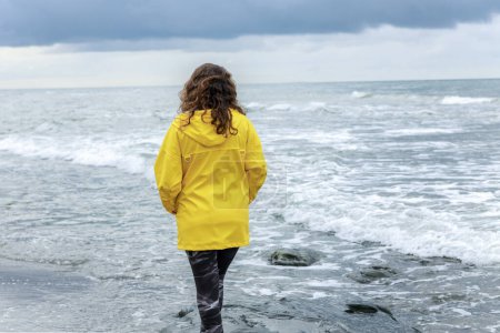 Téléchargez les photos : Jeune femme regardant vers l'horizon par la mer dans un temps nuageux pluvieux tempête - en image libre de droit