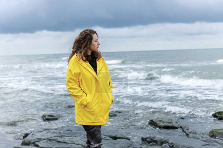 Foto de Mujer joven mirando hacia el horizonte por el mar en un clima lluvioso y nublado - Imagen libre de derechos