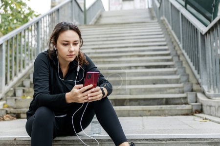 Téléchargez les photos : Jeune femme athlétique utilisant son téléphone intelligent avant de travailler - en image libre de droit